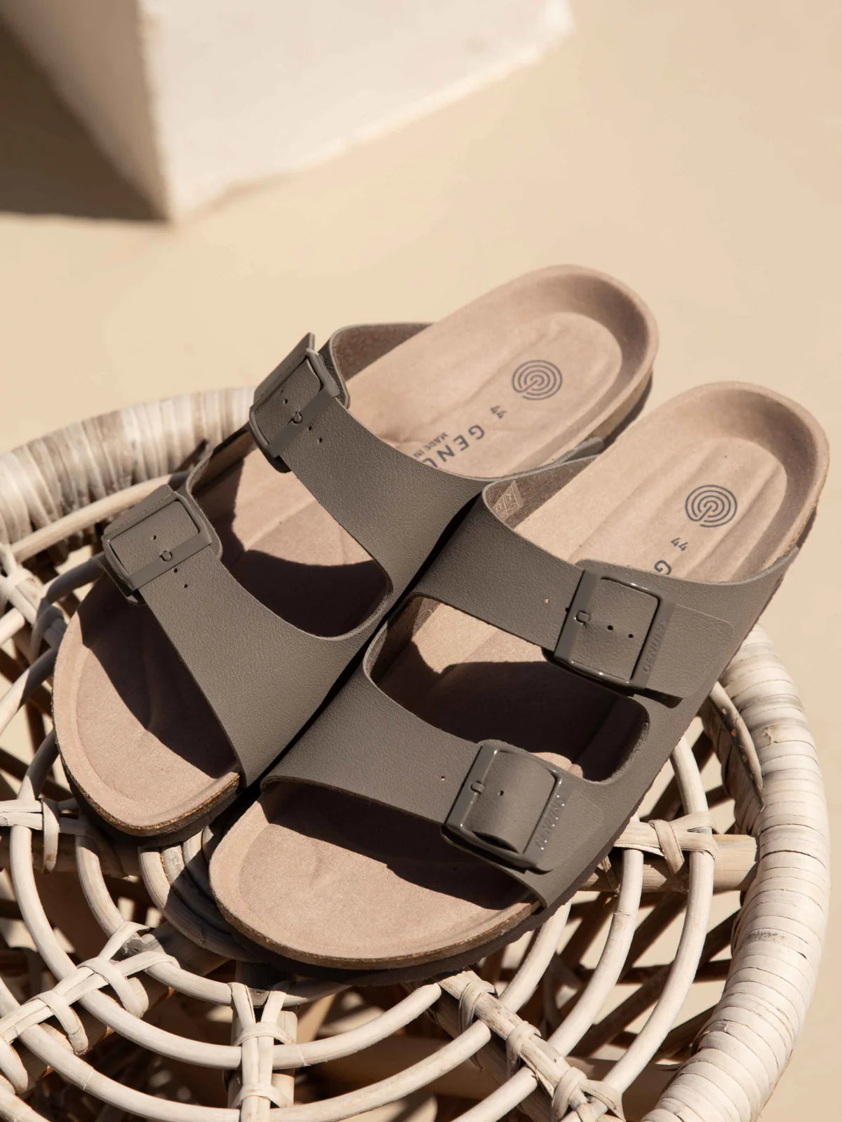 Pair of stone coloured genuins hawaii vegan sandals with a buckle on a woven surface.