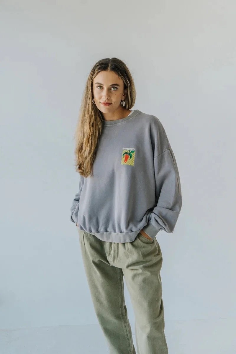 Woman wearing a bauy gray sweatshirt with a small pepper graphic on a plain background