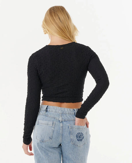 Person wearing a rip curl black long-sleeve crop top and light blue jeans on a white background