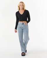 Woman wearing a rip curl black cropped cardigan and light blue jeans on a white background
