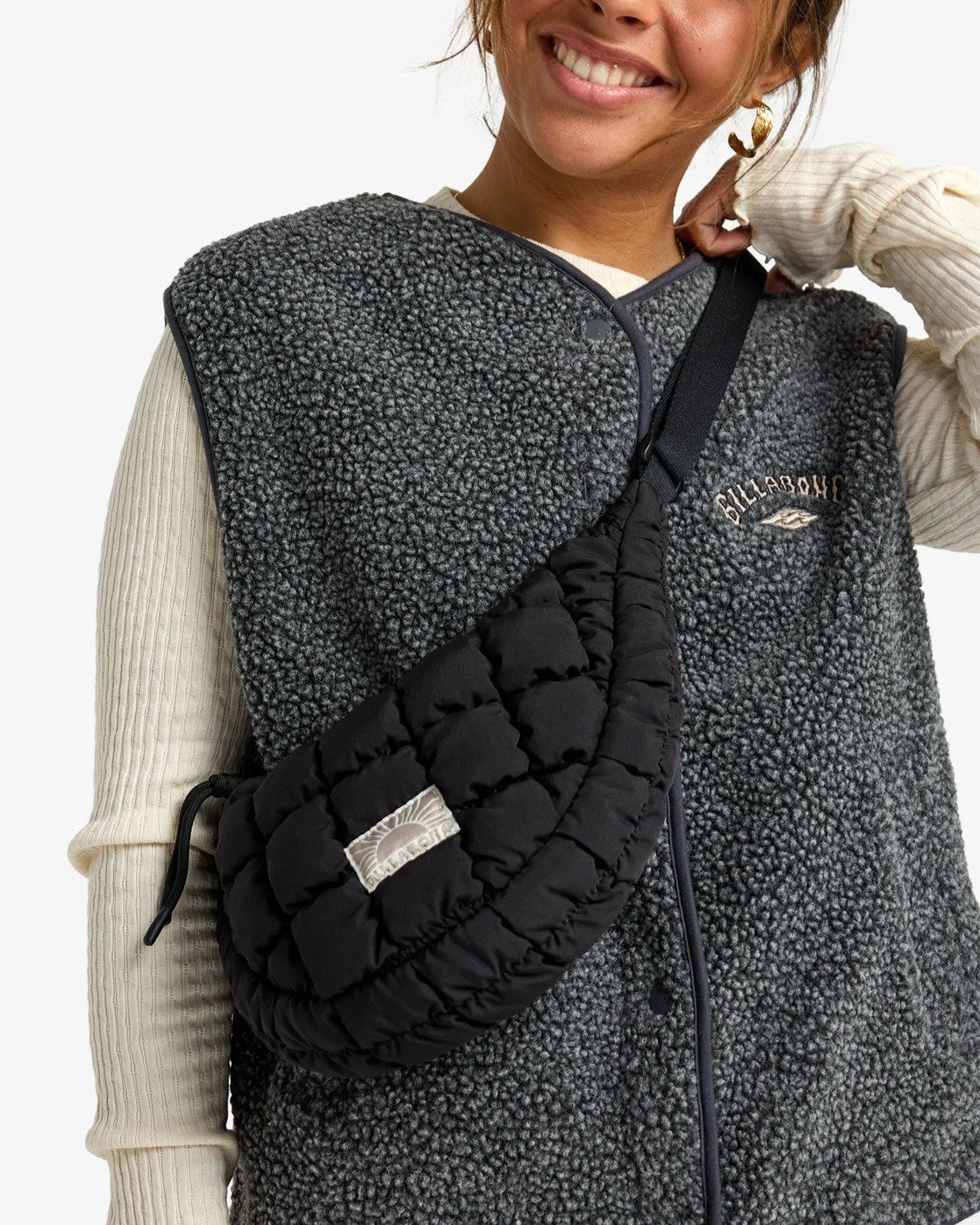 Person wearing a billabong black quilted bag over one shoulder with a gray fleece vest.