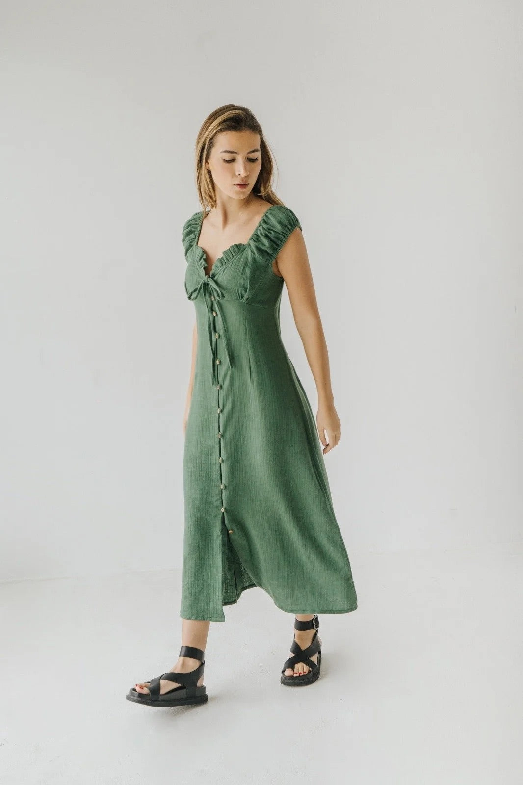 Woman wearing a bauy green midi dress on a plain background and genuins zaha embossed leather sandals