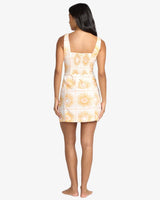 Woman wearing a white billabong dress with yellow floral patterns on a white background
