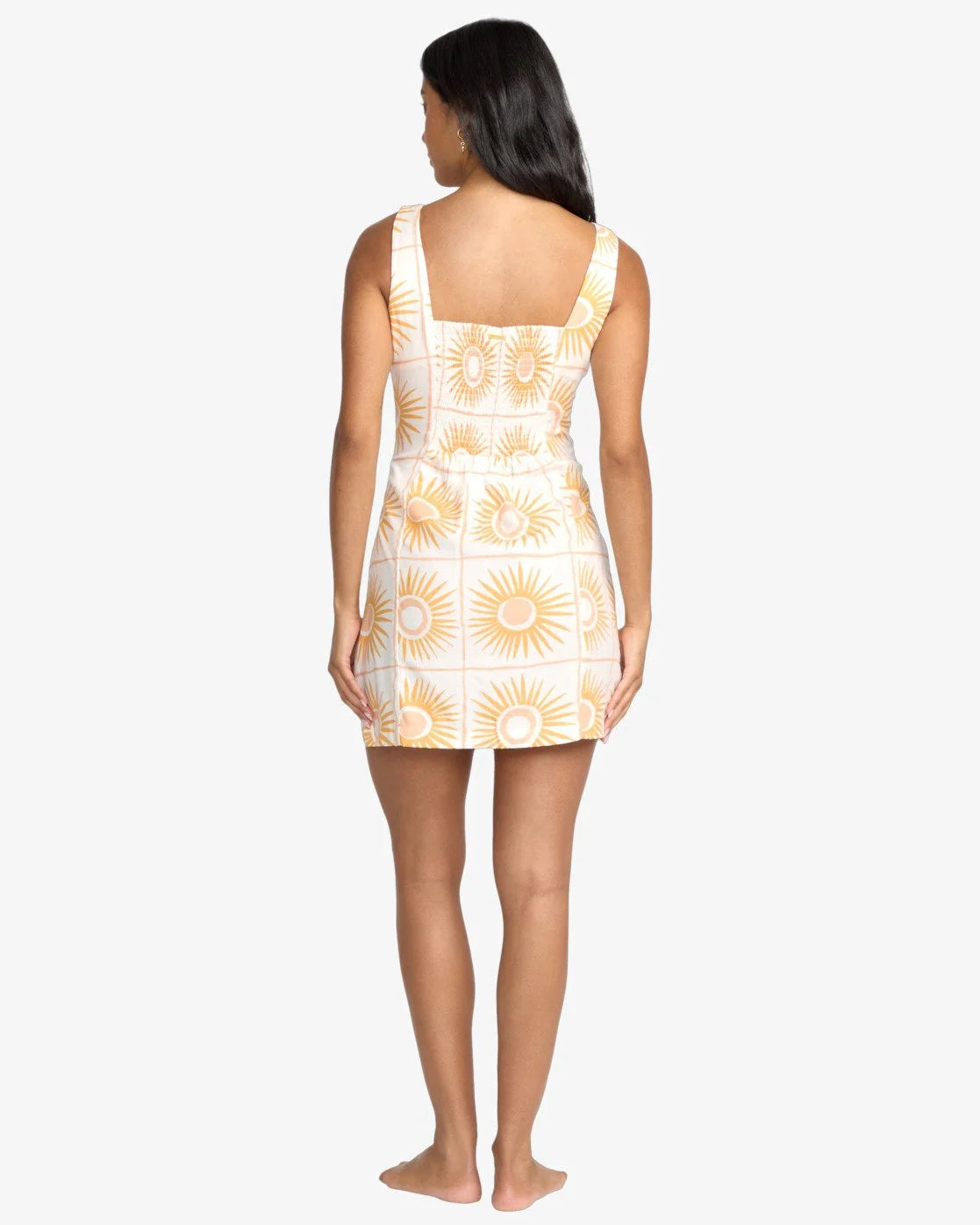 Woman wearing a white billabong dress with yellow floral patterns on a white background