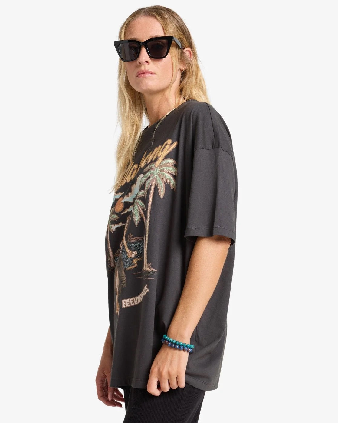 Woman wearing a billabong black oversized t-shirt with palm tree design on a white background