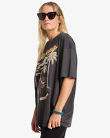 Woman wearing a billabong black oversized t-shirt with palm tree design on a white background