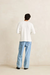 back of a man wearing a rhythm classic waffle knit white sweater and light blue jeans against a beige background