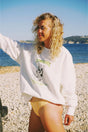 Woman wearing a white bauy cowgirl sweatshirt with a graphic design and yellow shorts on a pebbly beach.