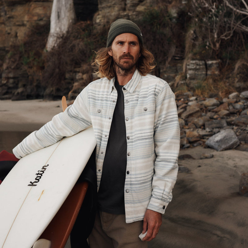 Man holding a surfboard on a rocky beach with cliffs in the background