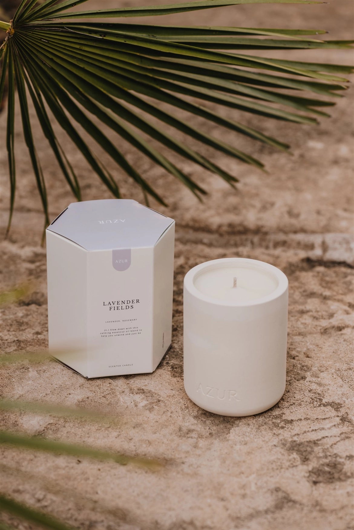 White candle and packaging on a textured surface with palm leaves in the background