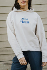 Person wearing a white Bauy mermaid hoodie with blue text against a wooden background