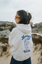 Person wearing a Bauy oversized hoodie with 'Mermaid on Rocks' design in a coastal setting