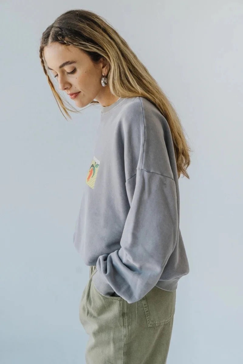 Woman wearing a light gray bauy pepper sweatshirt with a small graphic on a plain background