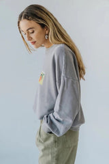 Woman wearing a light gray bauy pepper sweatshirt with a small graphic on a plain background