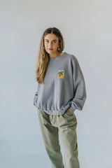 Woman wearing a bauy gray sweatshirt with a small pepper graphic on a plain background