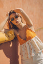 Woman wearing sunglasses and a yellow Bauy pineapple top against an orange wall