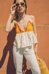 Woman wearing an orange Bauy pineapple top and white pants against a red wall