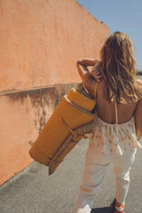 Woman with a yellow backpack walking along a street with an orange wall.