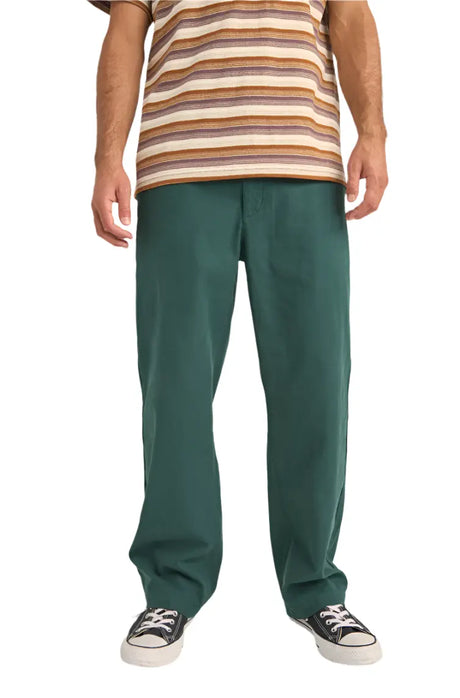 Person wearing rhythm essential twill green pants and a striped shirt on a white background