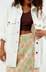 Person wearing a rhythm camilla oversized white denim jacket over a brown crop top and floral skirt.