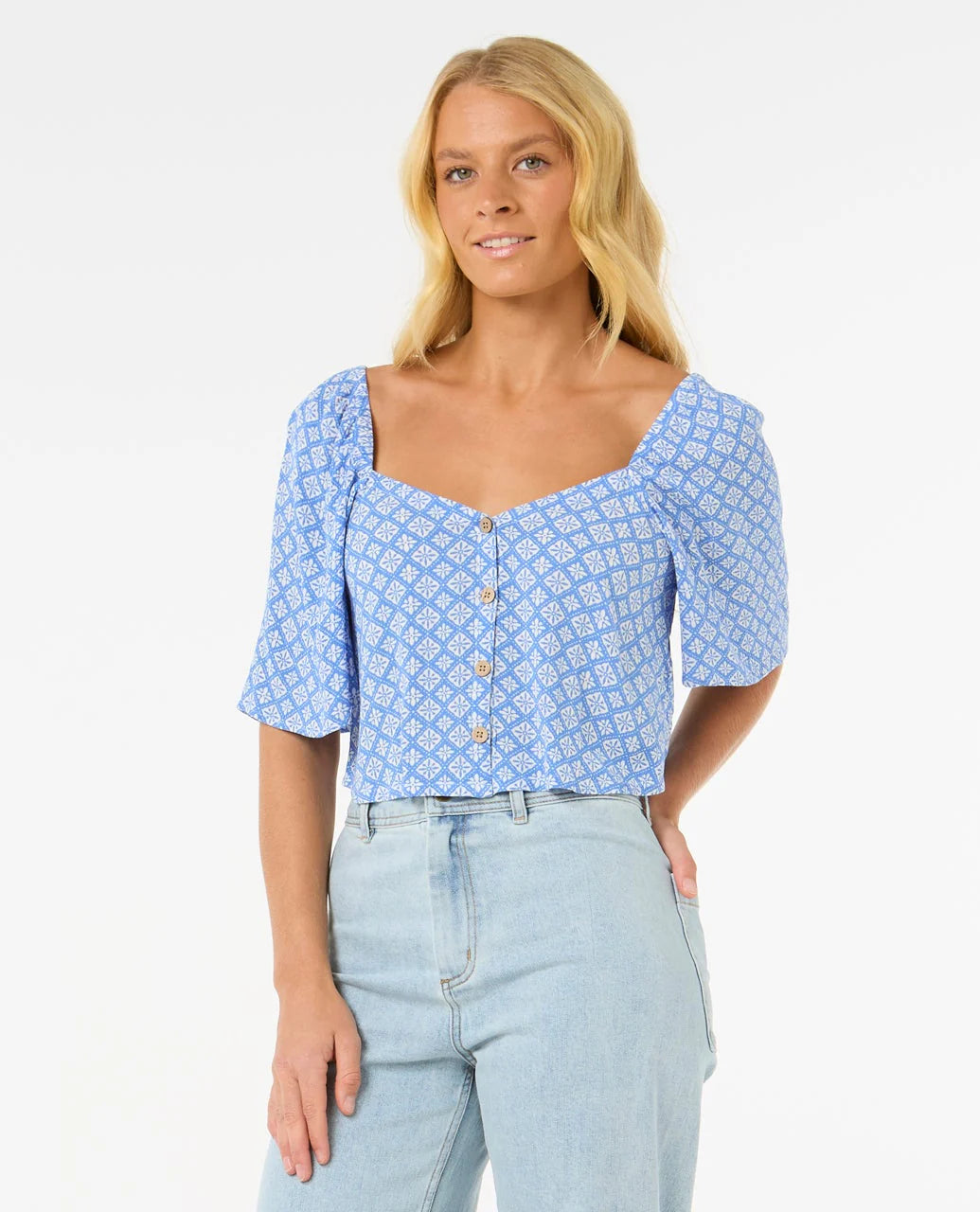 Woman wearing a rip curl blue patterned top and light blue jeans on a white background