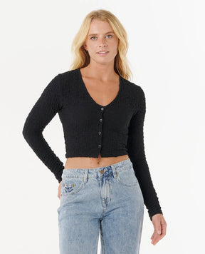 Woman wearing a rip curl black cropped cardigan and blue jeans on a white background