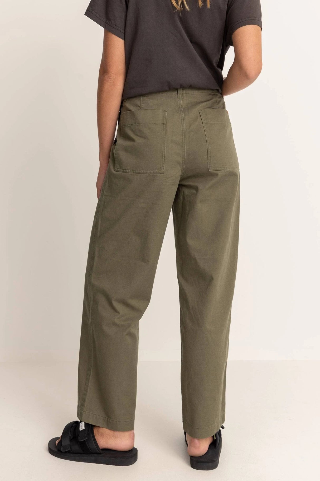 the back of a woman wearing rhythm fatigue olive green pants on a plain background