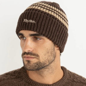 Man wearing a brown and beige beanie with 'Rhythm' logo on a white background